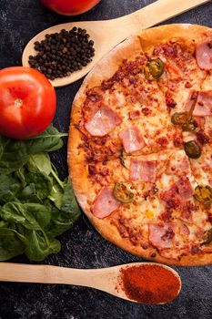 Top view on pizza, tomatoes, spinach and black pepper on dark wooden background