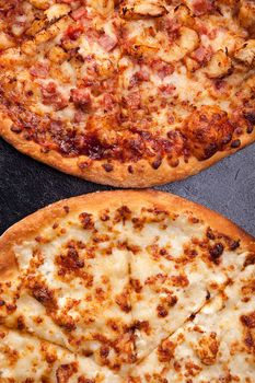 Top view of two pizza lying next to each other on dark wooden background