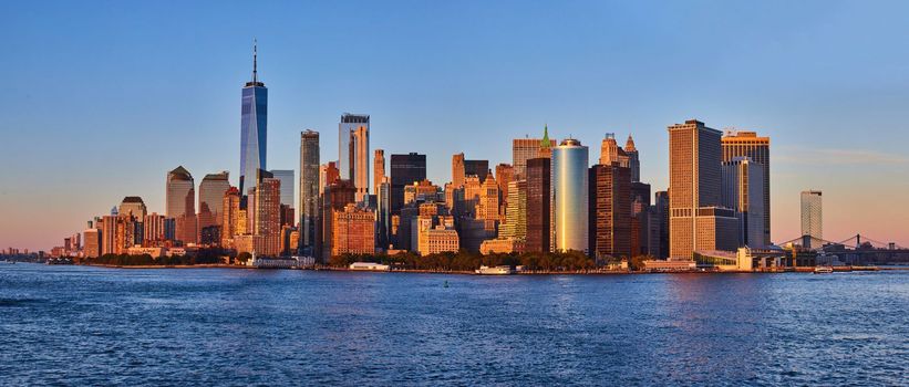 Image of Panoramic golden hour skyline of southern Manhattan New York City skyline from ferry with water in front