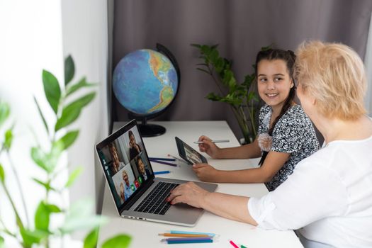 Happy mature grandmother with adorable little granddaughter using tablet at home together, excited middle aged woman and cute kid looking at device screen.