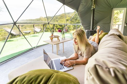 Happy young woman chatting online by using laptop in dome camping. Glamping vacation concept.