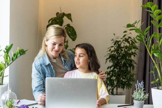 Beautiful mother and child looks at laptop screen spend time in kitchen using app education program, choose cartoons, teach kid pc usage, controls what daughter watching on internet cyberspace concept