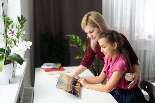 Beautiful young mother helping her younger daughter with homework.