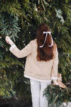 A girl with long hair stands with her back in a winter forest with a bouquet of fir branches. Snowy winter.