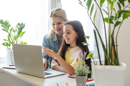 Beautiful mother and child looks at laptop screen spend time in kitchen using app education program, choose cartoons, teach kid pc usage, controls what daughter watching on internet cyberspace concept