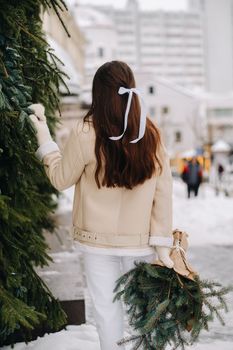 A girl with long hair stands with her back in the city with a bouquet of fir branches. Snowy winter.