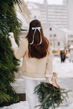 A girl with long hair stands with her back in the city with a bouquet of fir branches. Snowy winter.