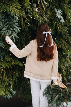 A girl with long hair stands with her back in a winter forest with a bouquet of fir branches. Snowy winter.