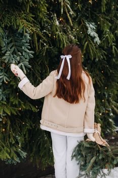 A girl with long hair stands with her back in a winter forest with a bouquet of fir branches. Snowy winter.