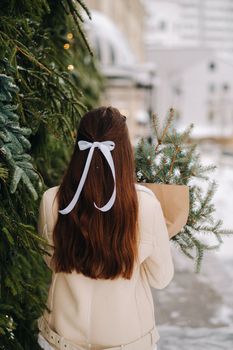 A girl with long hair stands with her back in the city with a bouquet of fir branches. Snowy winter.