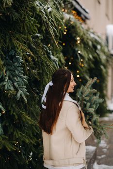 A girl with long hair stands with her back in a winter forest with a bouquet of fir branches. Snowy winter.