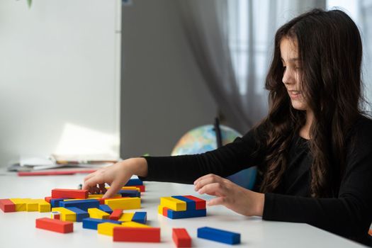 a little girl play a board game at the table. Construction of a tower from wooden cubes