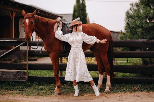 A girl in a white dress and a hat is standing next to a horse.