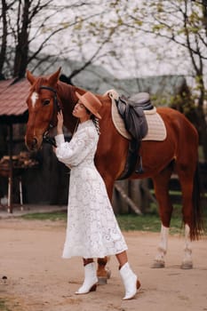 A girl in a white dress and a hat is standing next to a horse.
