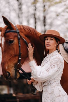 A girl in a white dress and a hat is standing next to a horse.