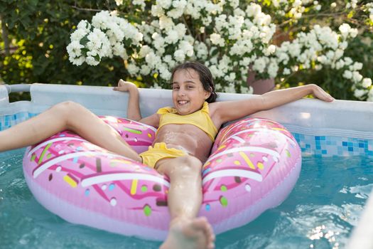 girl plays an inflatable ring is in swimming pool in the garden.