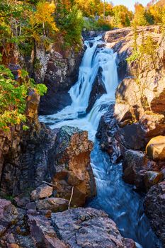 Image of Rocky cliff gorge canyon with large heavy waterfalls and fall forest