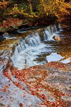 Image of Cascading small waterfalls in river with exposed rocks covered in fall leaves