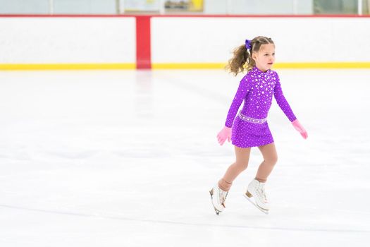 Little girl practicing figure skating on an indoor ice skating rink.