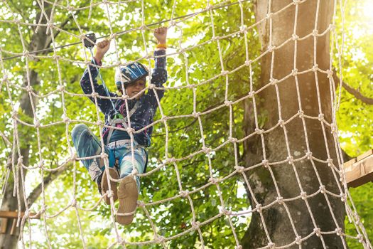 Little girl preschooler wearing full climbing harness having fun time in the rope park using carabiner and other safety equipment. Summer camp activity for kids. Adventure park in the forest.
