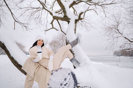 A beautiful girl with a beige cardigan and a white hat enjoying drinking tea in a snowy winter forest near a lake.