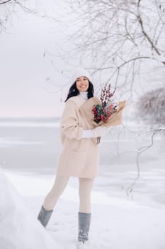 A girl in a beige cardigan and winter flowers walks in nature in the snowy season. Winter weather.