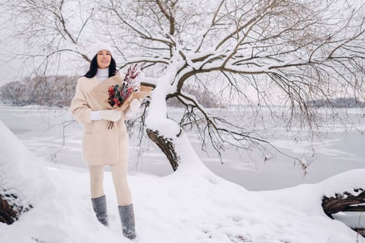 A girl in a beige cardigan and winter flowers walks in nature in the snowy season. Winter weather.