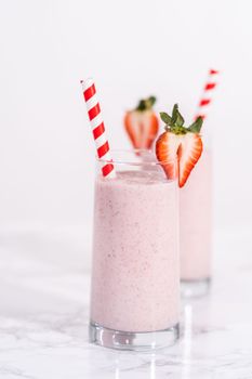 Freshly made healthy breakfast strawberry banana smoothie garnished with fresh strawberry and paper straw.