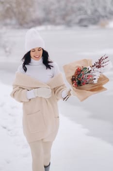A girl in a beige cardigan and winter flowers walks in nature in the snowy season. Winter weather.