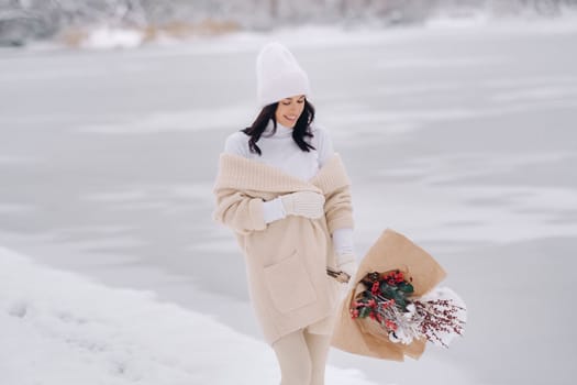 A girl in a beige cardigan and winter flowers walks in nature in the snowy season. Winter weather.