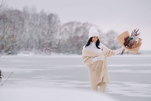 A girl in a beige cardigan and winter flowers walks in nature in the snowy season. Winter weather.