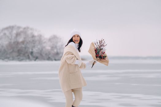 A girl in a beige cardigan and winter flowers walks in nature in the snowy season. Winter weather.