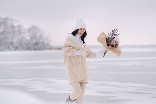 A girl in a beige cardigan and winter flowers walks in nature in the snowy season. Winter weather.