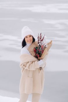 A girl in a beige cardigan and winter flowers walks in nature in the snowy season. Winter weather.