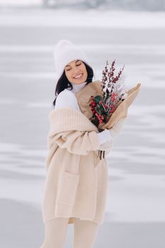 A girl in a beige cardigan and winter flowers walks in nature in the snowy season. Winter weather.