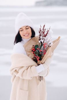 A girl in a beige cardigan and winter flowers walks in nature in the snowy season. Winter weather.