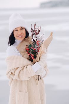 A girl in a beige cardigan and winter flowers walks in nature in the snowy season. Winter weather.