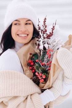 A girl in a beige cardigan and winter flowers walks in nature in the snowy season. Winter weather.