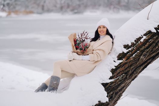 A girl in a beige cardigan and winter flowers walks in nature in the snowy season. Winter weather.