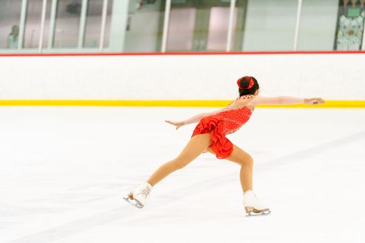 Teenage girl practicing figure skating on an indoor ice skating rink.