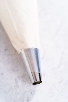 White buttercream frosting in a piping bag with a metal tip.