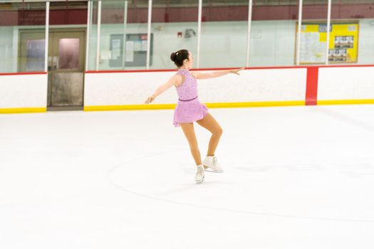 Teenage girl practicing figure skating on an indoor ice skating rink.