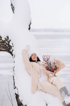 A beautiful girl in a beige cardigan and a white hat with flowers enjoys a snowy winter in nature.