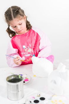 Little girl painting Halloween pumpkin with acrylic paint.