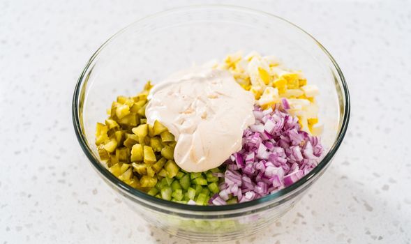 Mixing ingredients in a large glass mixing bowl to make potato salad.