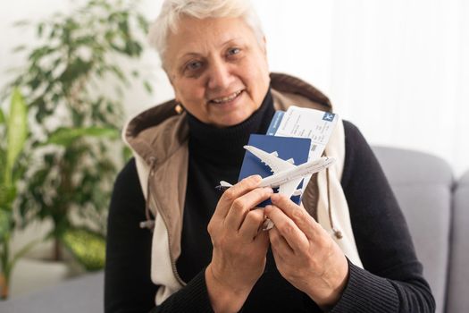 old woman holding Passport, boarding pass and toy airplane.