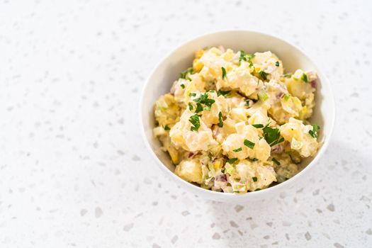 Serving potato salad garnished with fresh parsley in a white ceramic bowl.
