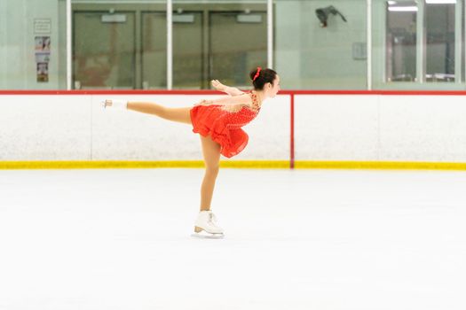 Teenage girl practicing figure skating on an indoor ice skating rink.