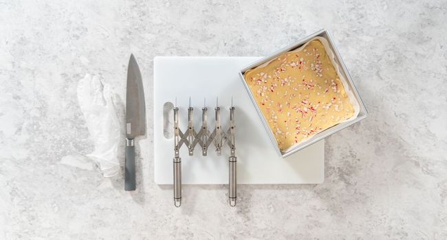 Flat lay. Removing candy cane fudge from a square cheesecake pan lined with parchment.