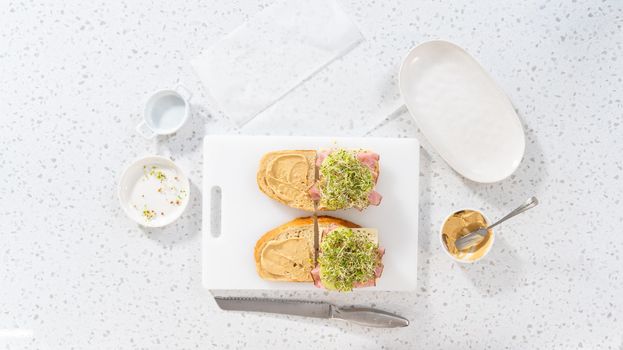 Flat lay. Assembling ham, cucumber, and sprout sandwiches on the white cutting board.